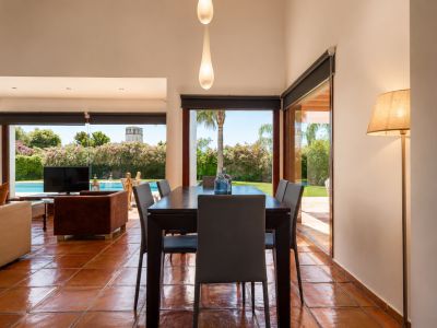 Der Essbereich mit dunklem Holztisch und Terrakottafliesen wird von Tageslicht durch große Glastüren erhellt. Er bietet direkten Blick auf den Garten, den Pool und einen entfernten Turm.