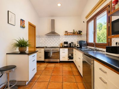 Funktionale Küche mit handgefertigtem Terrakottaboden, dunklen Arbeitsplatten und großen Holzfenstern, die viel Tageslicht hereinlassen.