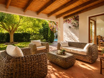 Geräumige überdachte Terrasse mit Holzbalkendecke und Terrakottafliesen, ausgestattet mit geflochtenen Outdoor-Möbeln und direktem Zugang zum Garten und Poolbereich.