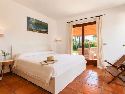 Helles Schlafzimmer mit weißem Bett, handgefertigten Terrakottaböden und direktem Zugang zur Außenterrasse mit Gartenblick.