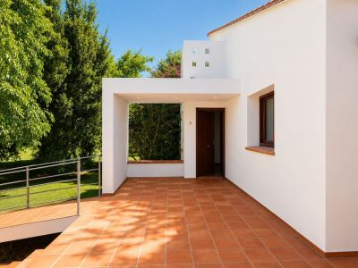 Überdachter Haupteingangsbereich mit Terrakotta-Fliesenboden und Einbauleuchten. Eine barrierefreie Rampe führt zum grünen Garten, ergänzt durch die weiße Fassade und Holztür.