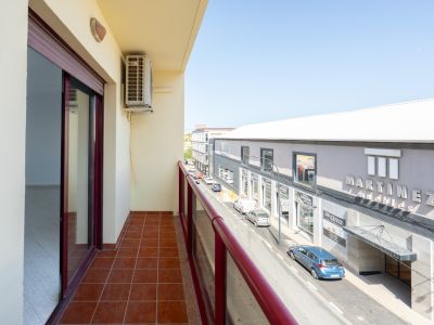 Außenbalkon mit Terrakottafliesen und rotem Geländer. Eine Klimaanlage ist sichtbar, mit Blick auf die Straße und das Geschäft "Martinez Muebles".
