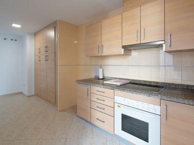Funktionale Küche mit hellen Holzschränken, Granit-Arbeitsplatte, integriertem Cerankochfeld und Backofen. Hoher Vorratsschrank und beige Bodenfliesen.