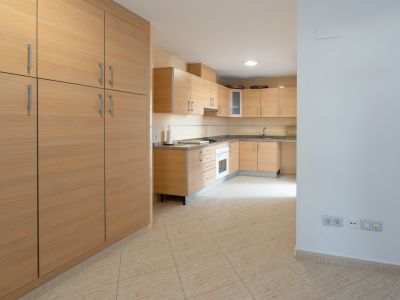 Geräumige Küche mit hellen Holzschränken, gesprenkelten Granitarbeitsplatten und integriertem Backofen. Ein großer passender Schrank steht links auf dem beigefarbenen Fliesenboden.
