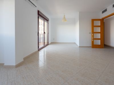 Geräumiger Raum mit beigem Keramikfliesenboden. Große Glasschiebetür (dunkelroter Rahmen) zur Terrasse, Split-Klimaanlage und helle Holztür mit satinierten Glasscheiben sind sichtbar.