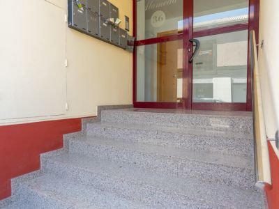 Granitähnliche Stufen führen zum Haupteingang des Gebäudes, mit einer dunkelrot gerahmten Glastür, beschriftet mit 'Edificio Alameda 36', und grauen Briefkästen an der linken Wand.
