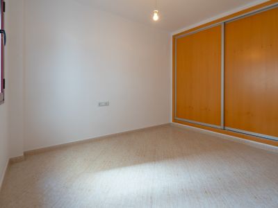 Helles Zimmer mit Einbauschrank, dessen Schiebetüren aus hellem Holz gefertigt sind, und beigefarbenem Fliesenboden. Ein Fenster mit dunklem Rahmen sorgt für Tageslicht.