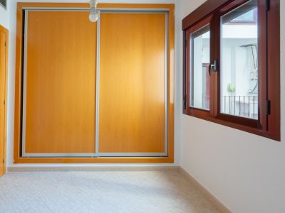 Nebenschlafzimmer mit geräumigem Einbauschrank mit hellen Holzschiebetüren und dunkelbraunem Holzfenster mit Blick auf einen Innenhof.