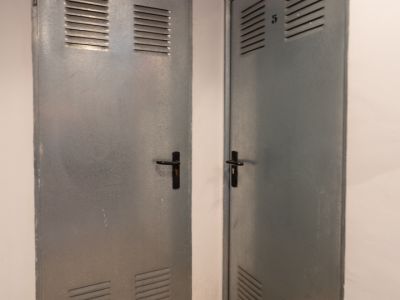 Zwei graue Metalltüren mit oberen und unteren Lüftungsschlitzen, eine mit 'Benissa Denia' beschriftet, die andere mit der Nummer '5', auf einem gesprenkelten Granitboden.
