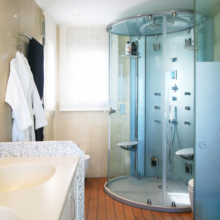 Badezimmer mit einer Glas-Duschkabine mit Massagedüsen, einem Waschtisch mit Kieselstein-Arbeitsplatte und warmem Holzfußboden. Natürliches Licht durch das Fenster.
