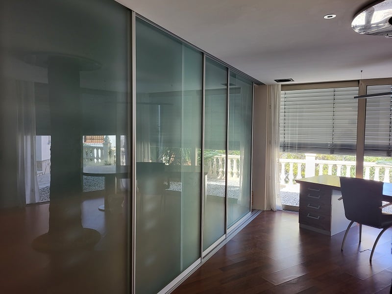 Büro oder Schlafzimmer mit eleganten Schiebetüren aus Milchglas, dunklem Holzboden und einem Arbeitsbereich am Fenster mit Blick auf die Balustrade.