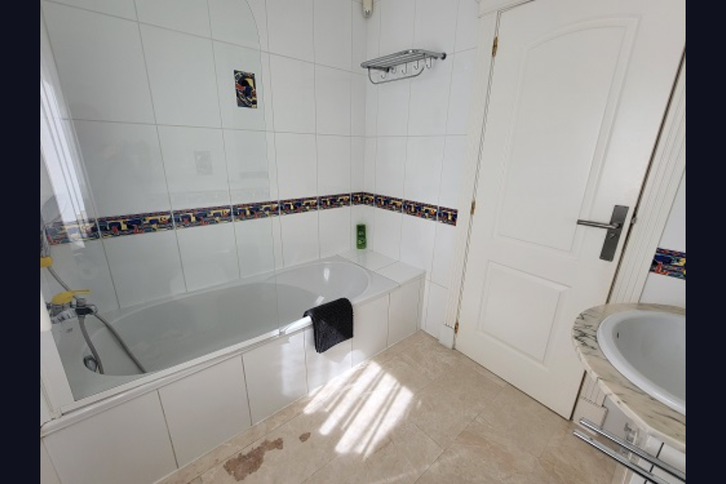 Funktionales Badezimmer mit weißer Badewanne, Glasduschwand und weißen Fliesenwänden mit Dekorstreifen. Ausgestattet mit Marmorwaschtisch und natürlichem Licht.