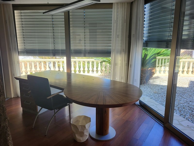 Geräumiges privates Büro mit großem Holzschreibtisch und Parkettboden. Die bodentiefen Fenster blicken auf eine Balustrade und einen mediterranen Garten.