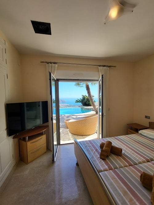 Helles Schlafzimmer mit Einzelbetten, Fernseher und direktem Zugang zur Terrasse. Es bietet einen weiten Blick auf den Infinity-Pool und das Mittelmeer.
