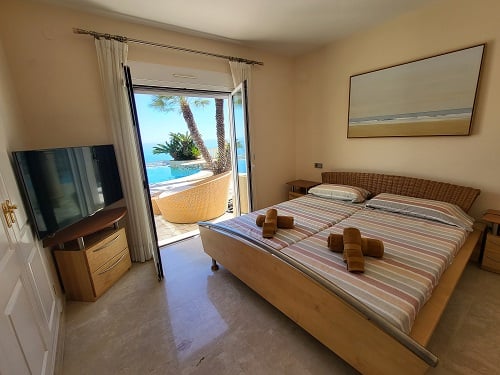 Helles Schlafzimmer mit Einzelbetten und geflochtenem Kopfteil, direktem Zugang zum Poolbereich und Meerblick. Mit Fernseher und Wandkunst.