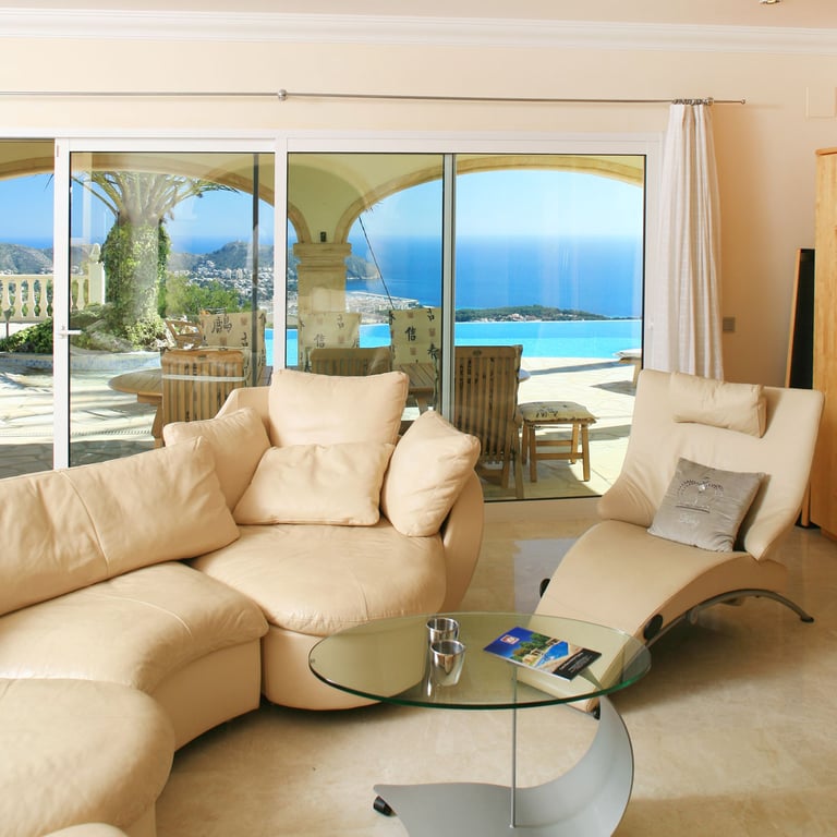 Helles Wohnzimmer mit geschwungenen, hellen Sofas und Marmorboden, das direkten Zugang zur Terrasse mit Infinity-Pool und Panoramablick auf das Meer bietet.