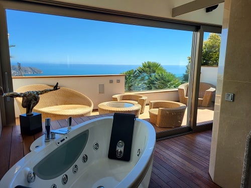 Innen-Whirlpool mit Holzboden, der sich zu einer privaten Terrasse mit Rattanmöbeln öffnet und einen Panoramablick auf das Mittelmeer bietet.