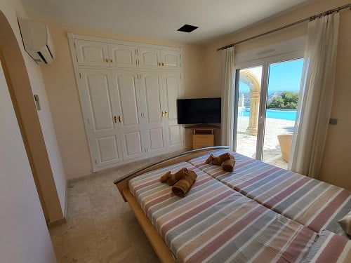 Schlafzimmer mit zwei Einzelbetten, Einbauschrank und direktem Zugang zum Poolbereich. Ausgestattet mit TV und Klimaanlage, bietet es Blick ins Freie.