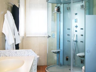 Badezimmer mit einer Glas-Duschkabine mit Massagedüsen, einem Waschtisch mit Kieselstein-Arbeitsplatte und warmem Holzfußboden. Natürliches Licht durch das Fenster.