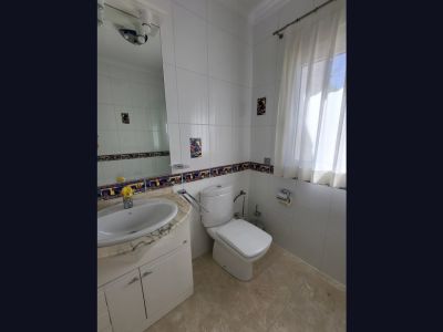 Badezimmer mit weißen Fliesenwänden und dekorativer Bordüre. Ausgestattet mit einem Waschtisch mit heller Marmorplatte, einer Toilette und einem Fenster mit transparenten Vorhängen.