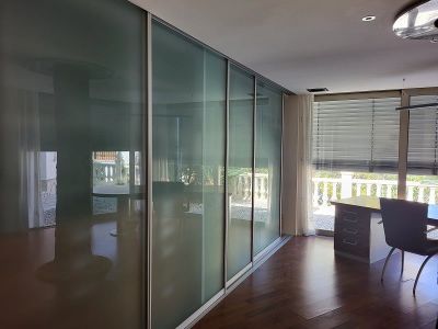 Büro oder Schlafzimmer mit eleganten Schiebetüren aus Milchglas, dunklem Holzboden und einem Arbeitsbereich am Fenster mit Blick auf die Balustrade.