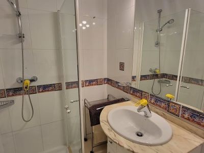 Funktionales Badezimmer mit Glasduschkabine, Waschtisch mit heller Marmorplatte und beleuchtetem Spiegel. Weiße Fliesen mit dekorativer mediterraner Bordüre.