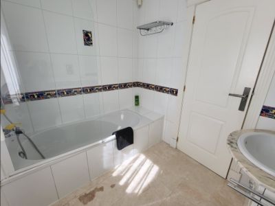 Funktionales Badezimmer mit weißer Badewanne, Glasduschwand und weißen Fliesenwänden mit Dekorstreifen. Ausgestattet mit Marmorwaschtisch und natürlichem Licht.