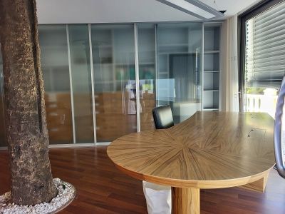 Geräumiges privates Büro mit einem einzigartigen Holzschreibtisch, Milchglas-Schiebetüren, einem Innenbaum und viel Tageslicht durch das große Fenster.