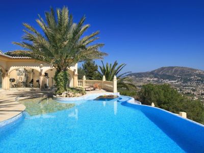 Geschwungener Mosaikpool mit Palmeninsel und Unterwassertisch. Verglaster Fitnessbereich und Terrasse mit Panoramablick auf die Berge.