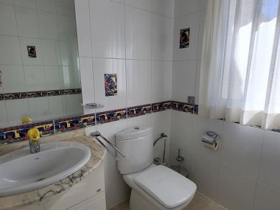 Helles Badezimmer mit weißen Wandfliesen, farbiger Dekorleiste und Akzentstücken. Ausgestattet mit Marmorwaschtisch, integriertem Waschbecken, moderner Toilette und Fenster mit Gardine.
