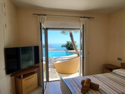 Helles Schlafzimmer mit Einzelbetten, Fernseher und direktem Zugang zur Terrasse. Es bietet einen weiten Blick auf den Infinity-Pool und das Mittelmeer.