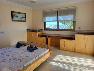 Helles Schlafzimmer mit hellem Holzdoppelbett, integriertem Schreibtisch und Schränken. Die Fenster bieten Panoramablicke auf die Küste und füllen den Raum mit Tageslicht.