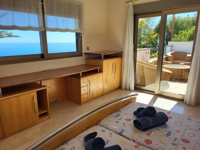 Helles Schlafzimmer mit zwei Einzelbetten, integriertem Holzschreibtisch und weitem Meerblick. Direkter Zugang zu einer privaten Terrasse mit Sitzgelegenheiten.