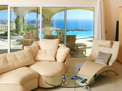 Helles Wohnzimmer mit geschwungenen, hellen Sofas und Marmorboden, das direkten Zugang zur Terrasse mit Infinity-Pool und Panoramablick auf das Meer bietet.