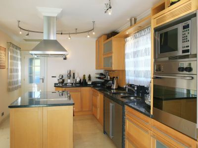 Moderne Küche mit hellen Holzschränken, dunklen Granitarbeitsplatten und einer Kochinsel mit integriertem Kochfeld. Edelstahlgeräte umfassen Backofen, Mikrowelle und Dunstabzugshaube.