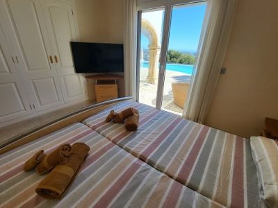 Schlafzimmer mit zwei Einzelbetten, Einbauschrank und Wandfernseher. Direkter Zugang zum Außenpoolbereich mit Bogen und freier Aussicht.