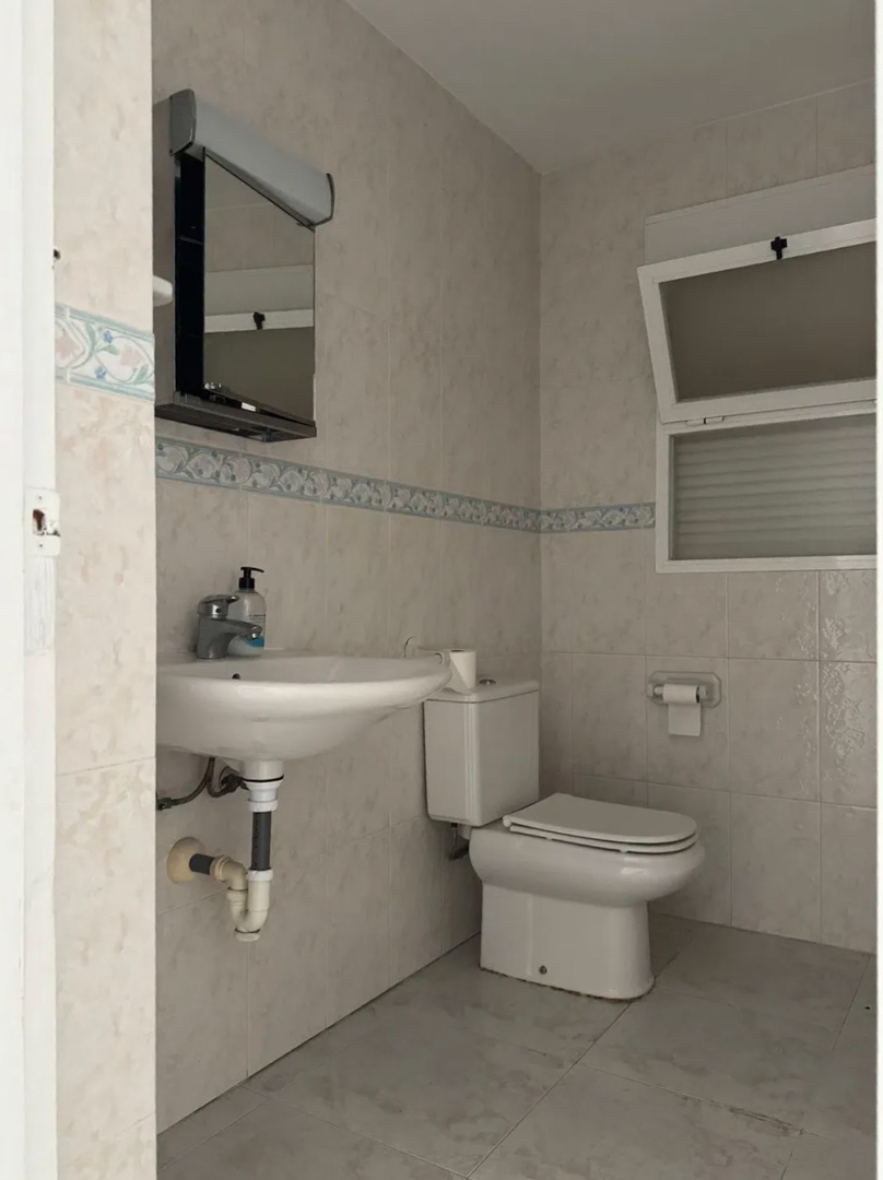 Funktionales Badezimmer mit hellen Fliesen, dekorativer Bordüre und Kippfenster. Ausgestattet mit Hängewaschbecken, Toilette und Spiegelschrank mit Beleuchtung.
