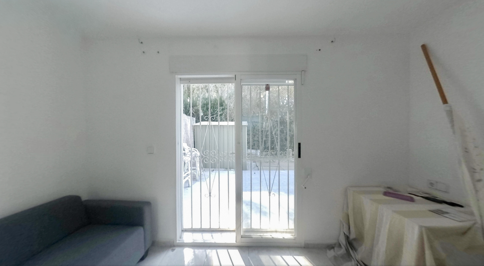 Geräumiger Raum mit Glasschiebetüren und Sicherheitsgittern, direktem Zugang zum privaten Garten und viel Tageslicht auf dem hellen Boden.