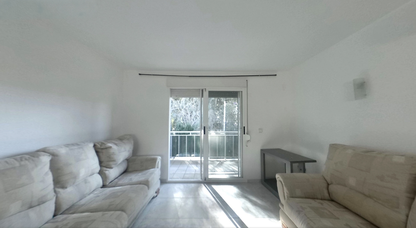 Helles Wohnzimmer mit hellen Sofas, Fliesenboden und Glasschiebetüren, die auf einen Balkon führen und den Raum mit Tageslicht durchfluten.