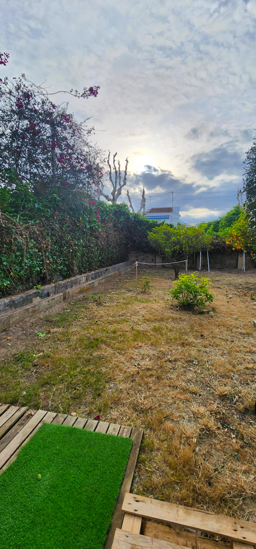 Hinterer Garten mit offenem Gelände, Obstbäumen und blühender Hecke. Im Vordergrund eine Holzbasis mit Kunstrasen. Ideal zur Personalisierung und für einen Pool.