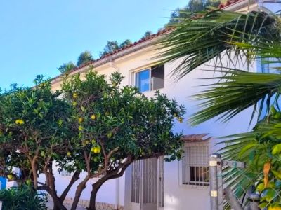 Außenansicht der weißen Villa mit Ziegeldach und Zitrusbäumen voller gelber Früchte. Eine Eingangstür und Fenster sind deutlich zu erkennen.