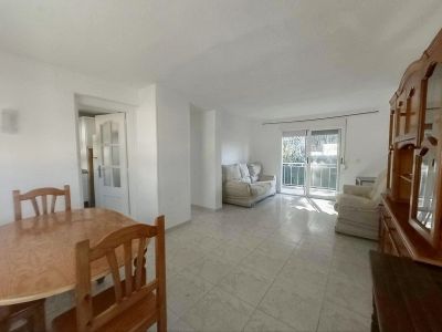 Blick auf den hellen Wohn-Essbereich mit ovalem Holztisch, Fliesenboden und großem Holzschrank. Glasschiebetüren führen zu einem Balkon und durchfluten den Raum mit natürlichem Licht.