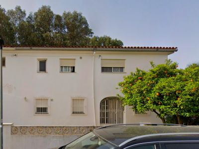 Die weiße Fassade der zweistöckigen Villa zeigt ein Ziegeldach, einen gewölbten Eingang mit Ziergitter und Fenster mit Gittern. Ein reifer Orangenbaum, voll mit Früchten, steht prominent davor.