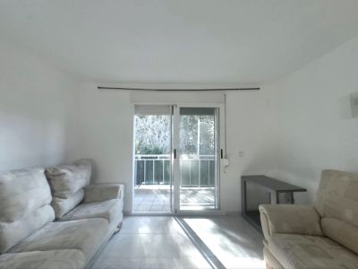 Helles Wohnzimmer mit hellen Sofas, Fliesenboden und Glasschiebetüren, die auf einen Balkon führen und den Raum mit Tageslicht durchfluten.