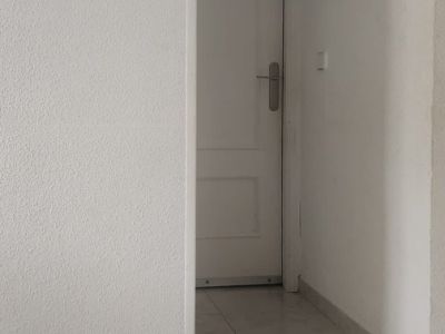 Innenflur mit hellen Fliesen und weißen strukturierten Wänden, der zu einer Kassettentür führt, mit einer kleinen Wanddekoration.