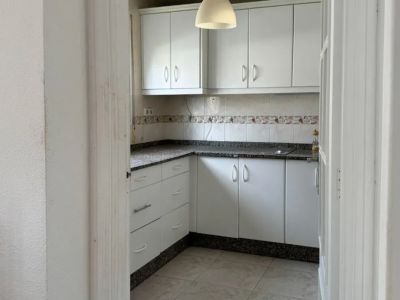 Kompakte Küche mit weißen Schränken, dunklen gesprenkelten Granitarbeitsplatten und einem dekorativen Fliesenspiegel. Der Raum wird durch eine zentrale Pendelleuchte und helle Bodenfliesen beleuchtet.