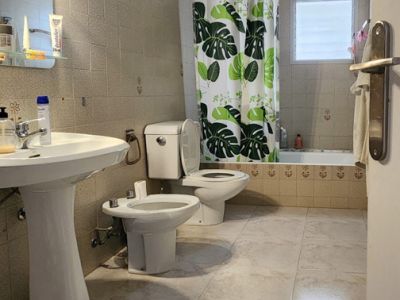 Praktisches Badezimmer mit hellen Marmor-Effekt-Bodenfliesen und beigefarbenen Wandfliesen. Ausgestattet mit Standwaschbecken, WC, Bidet und Badewanne mit Duschvorhang und Milchglasfenster.