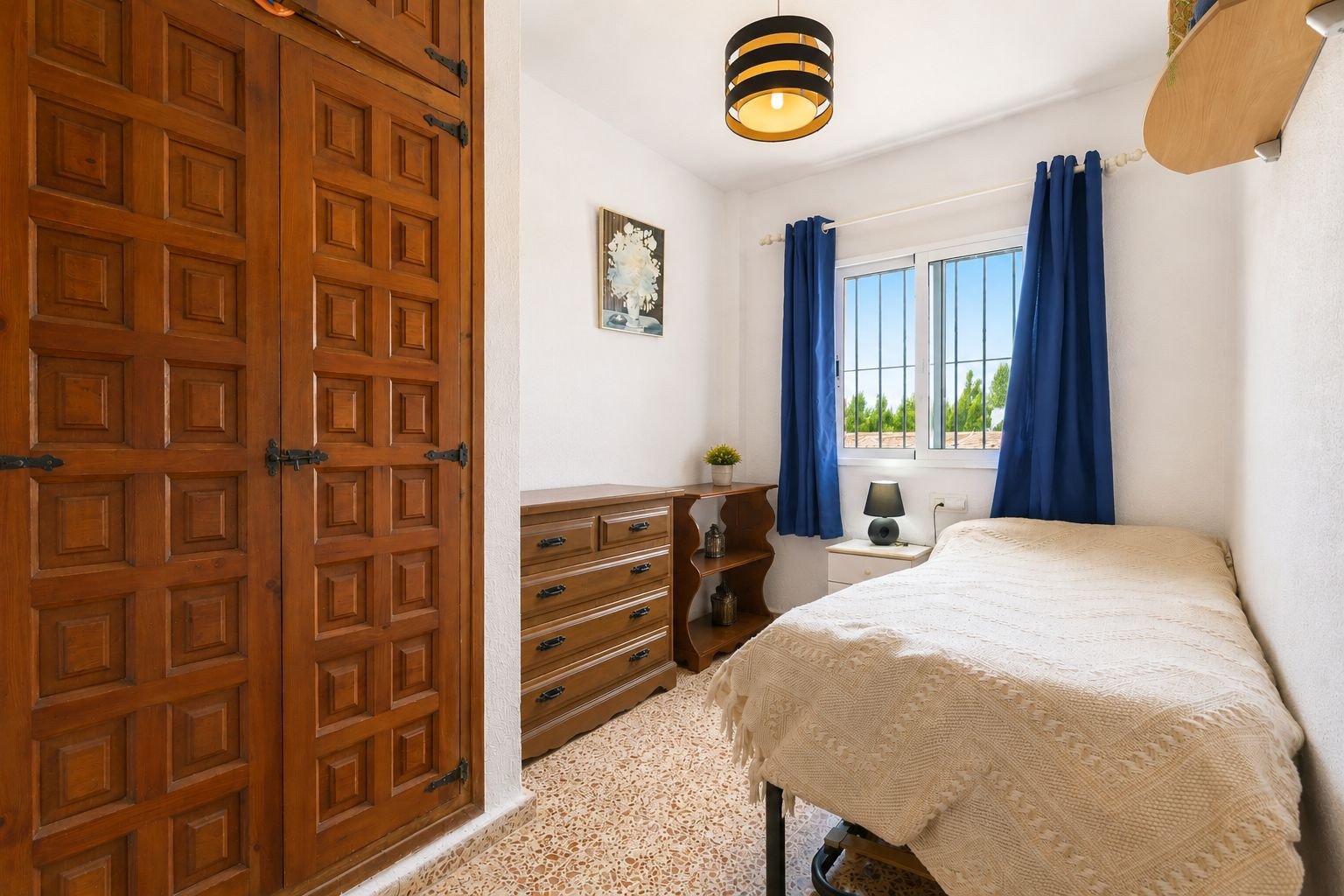 Gemütliches Schlafzimmer mit markantem Einbauschrank aus Holz, Zierpaneelen und schwarzen Beschlägen. Fenster mit blauen Vorhängen bietet Tageslicht und Blick ins Grüne. Gemütliches Schlafzimmer mit markantem Einbauschrank aus Holz, Zierpaneelen und schwarzen Beschlägen. Fenster mit blauen Vorhängen bietet Tageslicht und Blick ins Grüne.