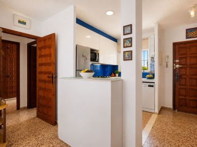 Der Eingangsbereich zeigt charakteristische gemusterte Bodenfliesen und klassische Holztüren. Eine moderne Küche mit blauem Fliesenspiegel und weißen Schränken ist durch eine Trennwand sichtbar.