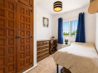 Gemütliches Schlafzimmer mit markantem Einbauschrank aus Holz, Zierpaneelen und schwarzen Beschlägen. Fenster mit blauen Vorhängen bietet Tageslicht und Blick ins Grüne.